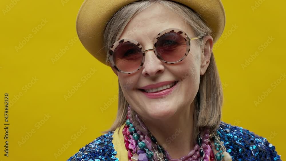 Stylish Elderly Woman On Yellow Background. She Is Wearing Hat And Glasses. Stylish Elderly Woman On Yellow Background. She Is Wearing Hat And Glasses.