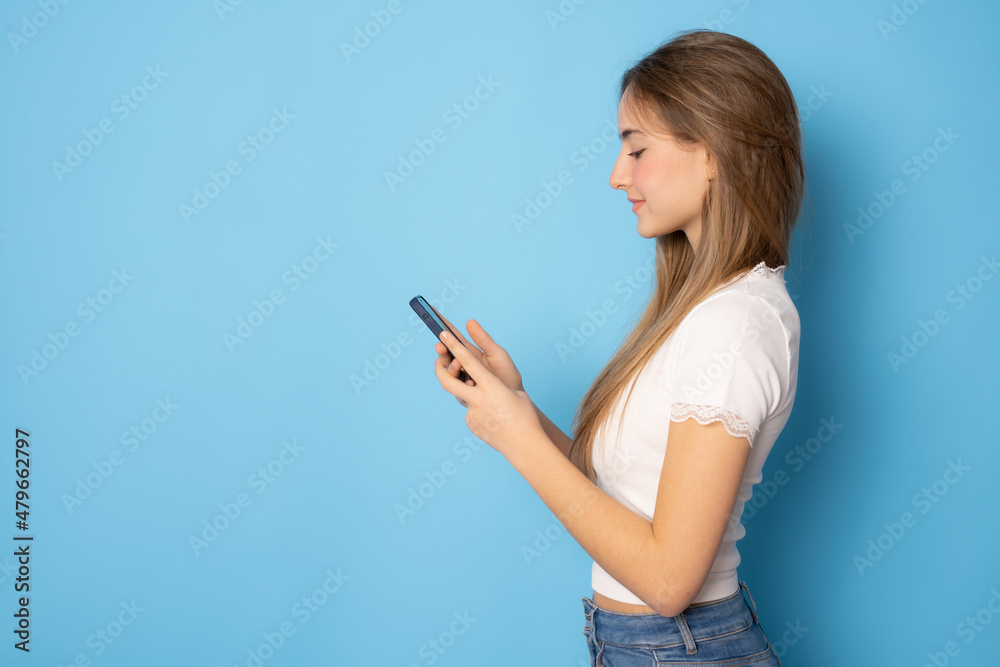 Beautiful girl using smartphone standing isolated over blue background. Beautiful girl using smartphone standing isolated over blue background.