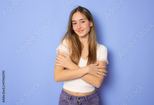 Beautiful young woman in casual clothing hugging herself over purple background. © Danko