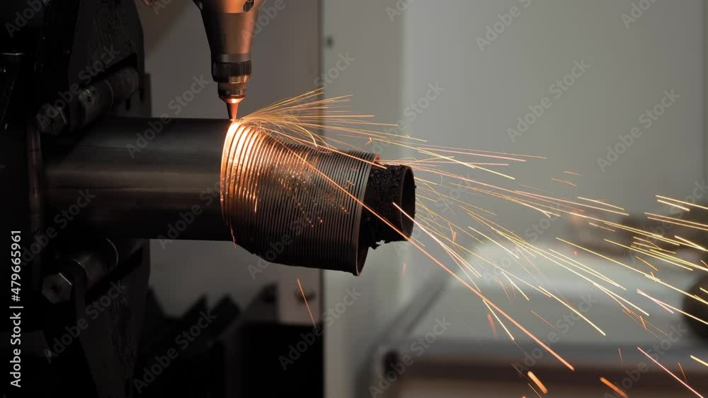 Close up, side view: automatic cnc laser cutting machine working with cylindrical metal workpiece with many sparks at factory. Metalworking, industrial, manufacturing, technology and equipment concept Close up, side view: automatic cnc laser cutting machine working with cylindrical metal workpiece with many sparks at factory. Metalworking, industrial, manufacturing, technology and equipment concept