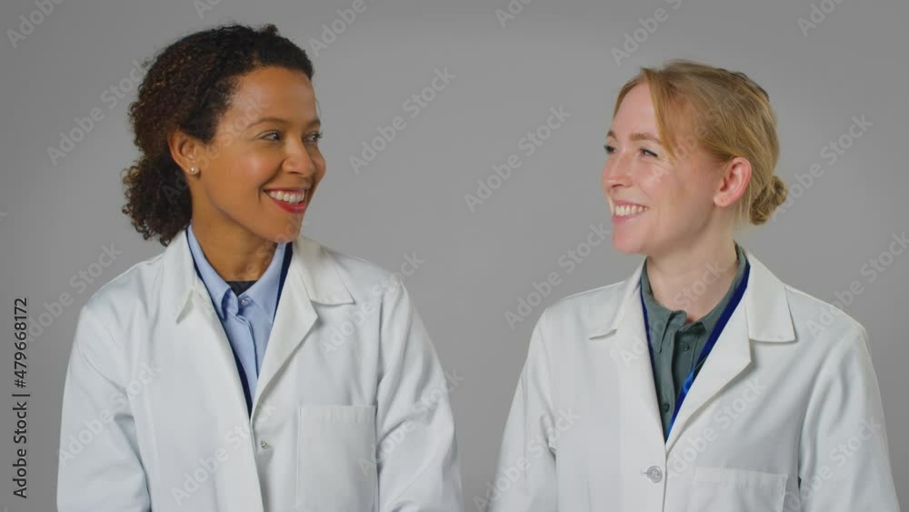 Studio Portrait Of Two Smiling Female Doctors Or Lab Workers In White Coats Studio Portrait Of Two Smiling Female Doctors Or Lab Workers In White Coats