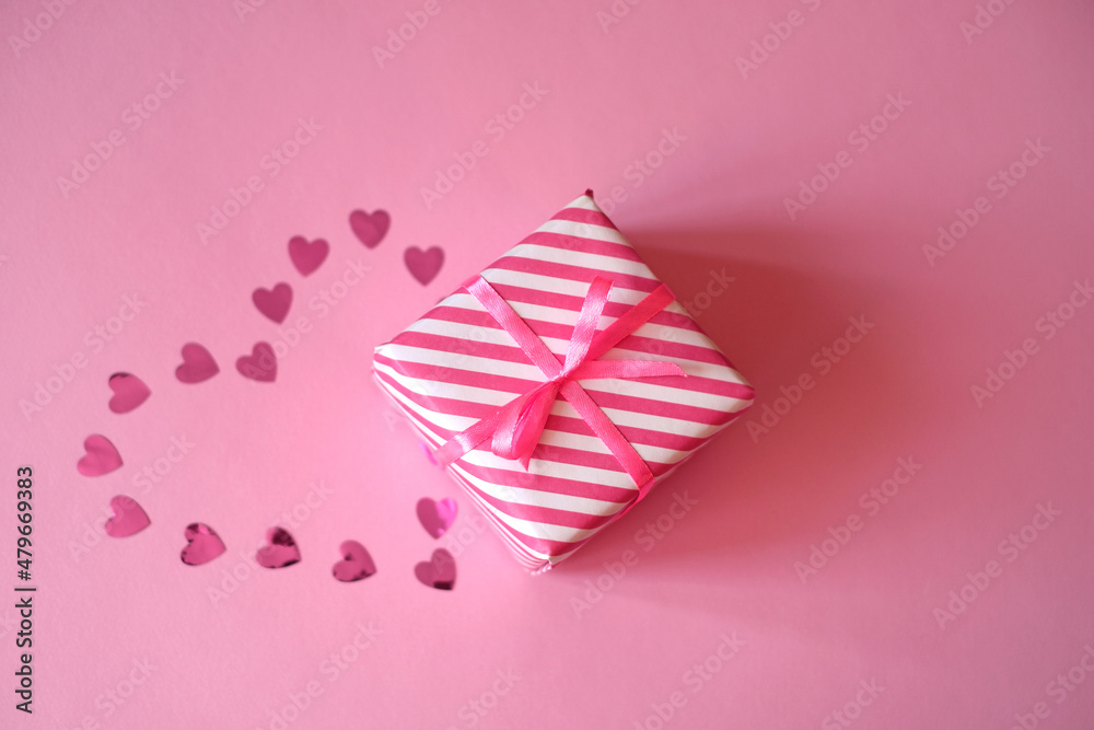 Obraz premium A pink confetti heart is laid out on a background next to a gift box tied with a ribbon with a bow. A valentine's Day gift. Give presents for the holidays