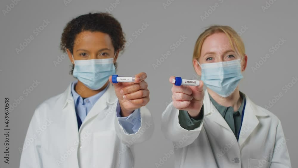 Studio Shot Of Lab Research Workers In Face Masks Holding Test Tubes Labelled Covid-19 And Vaccine Studio Shot Of Lab Research Workers In Face Masks Holding Test Tubes Labelled Covid-19 And Vaccine