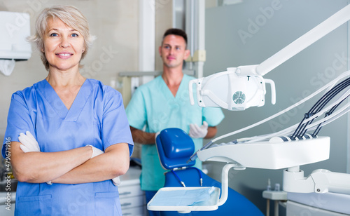 Portrait of cheerful woman dentist arms crossed with dental assistant behind in the dental clinic