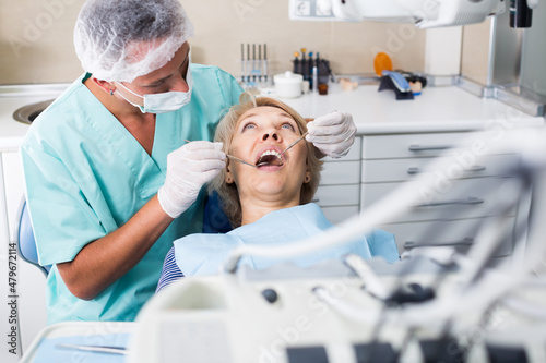Professional dentist examining and performing treatment to mature woman
