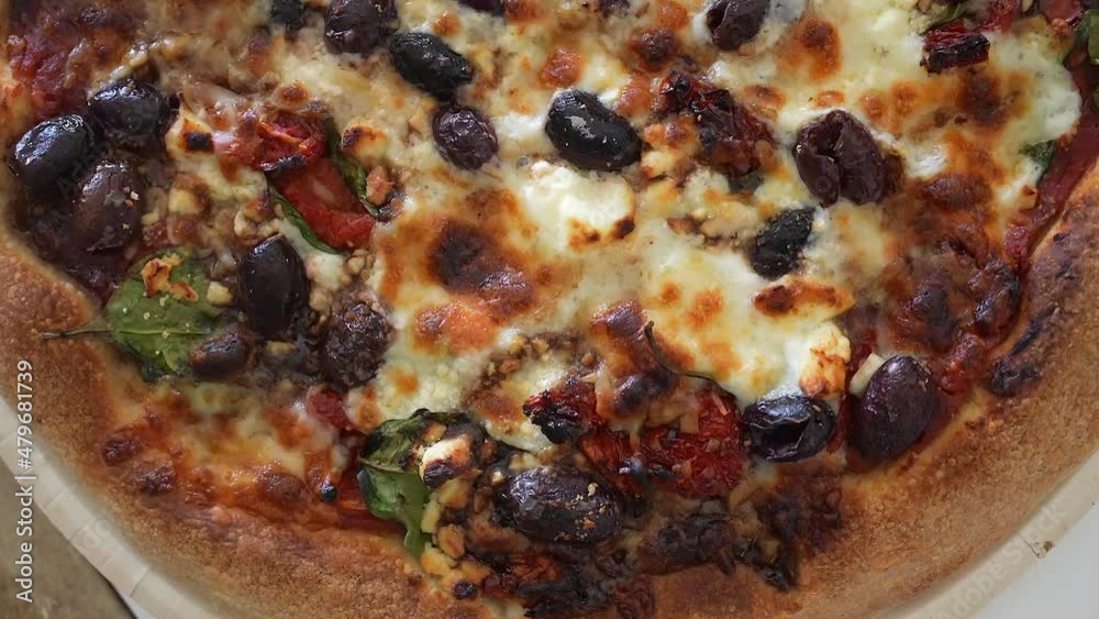 Overhead sliding view of freshly baked combination pizza with black olives, tomatoes, peppers and other ingredients baked in the cheese