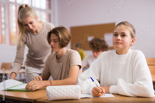 Diligent teenage high school students studying in college with classmates, making notes of teacher lecture