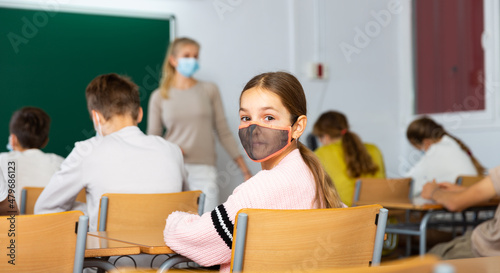 Student in protective mask studying in classroom, listening to lecturer and writing in notebook. High quality photo