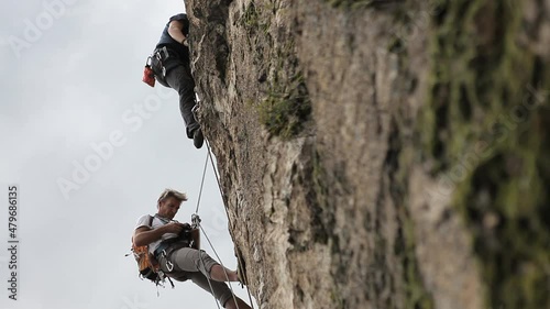 Climbers ascend a rugged rock face with mountains behind