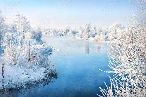 Trees on the bank of a blue river in white snow frost in the Moscow region on a winter sunny evening photo