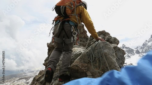 Climbers ascend a rugged rock face with mountains behind