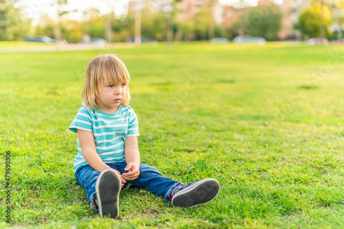 little boy sitting on grass of a park looking away