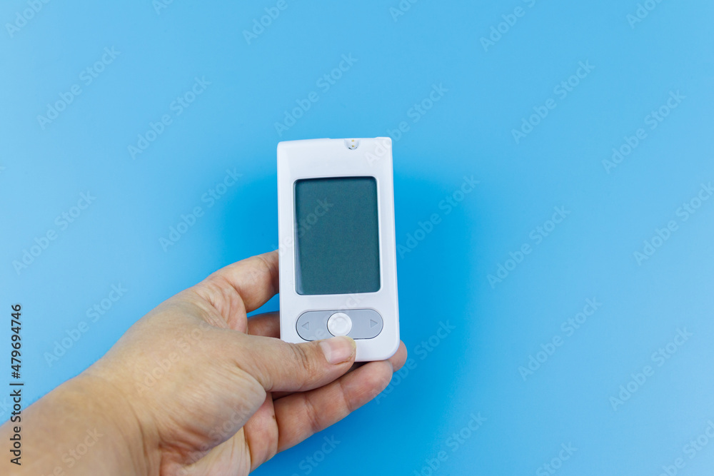 Digital glucometer in female hand over a pastel blue background. Diabetes concept Digital glucometer in female hand over a pastel blue background. Diabetes concept