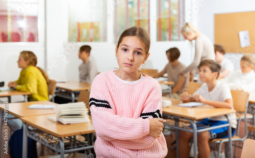 Upset girl stands in a school class against the background of classmates