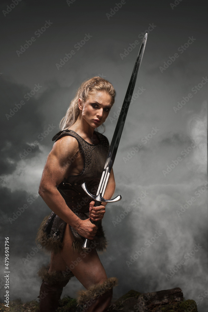 Fantasy woman warrior in laether armor stained with blood and mud, holding sword. Cosplayer historical viking