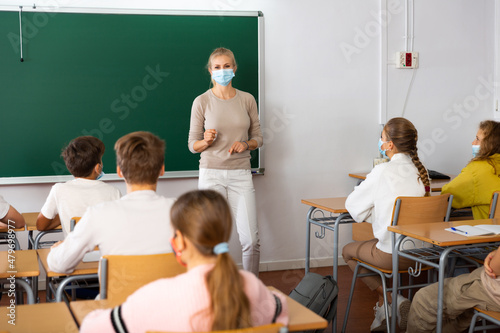 Woman teacher in face mask explaining new theme to children during class in primary school indoors