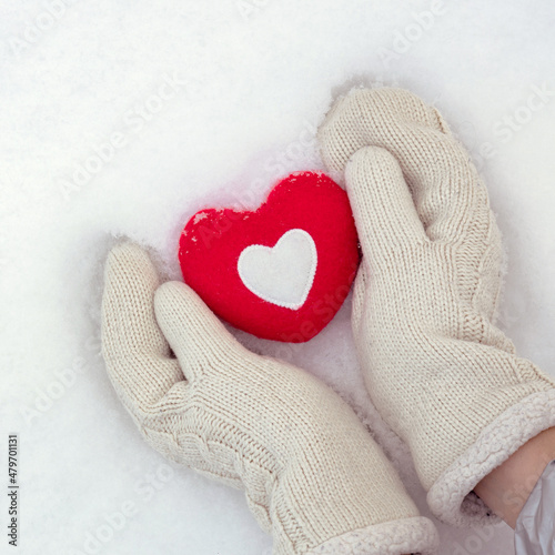 winter love background, hands in knitted mittens hold a red heart on fresh snow