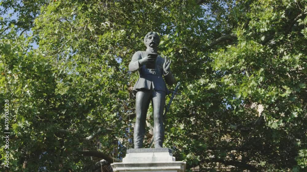 Cast iron statue of male historical figure reading announcement against leafy green backdrop. Slow zoom out. Cast iron statue of male historical figure reading announcement against leafy green backdrop. Slow zoom out.