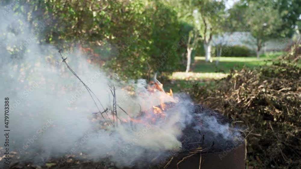 Dry leaves and branches burning in a barrel with thick smoke, windy weather, static and tilt down Dry leaves and branches burning in a barrel with thick smoke, windy weather, static and tilt down