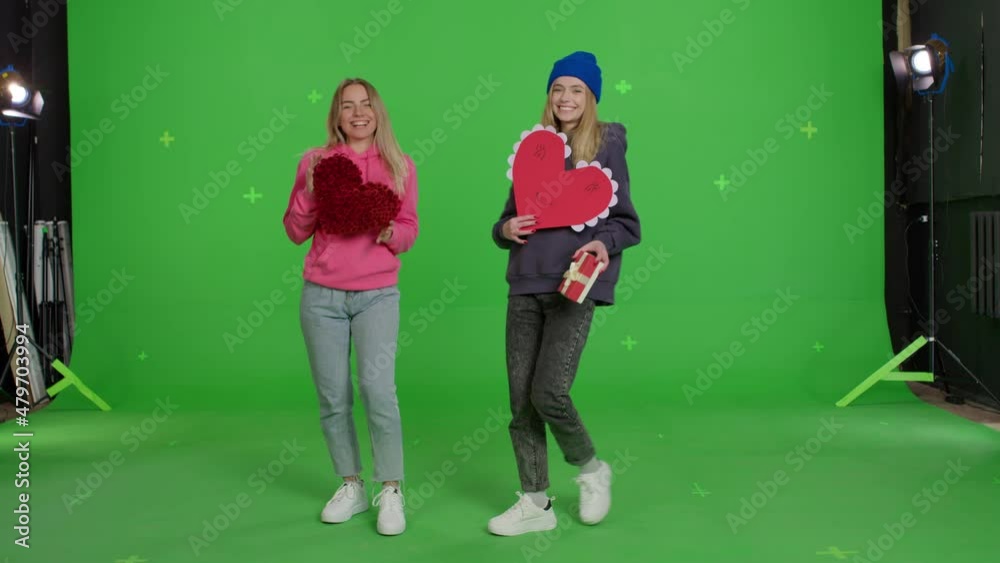 Two girls enter with valentines in their hands, dance. Friendship love and valentine's day. Young caucasian women having fun in front of green screen background. Chroma key Two girls enter with valentines in their hands, dance. Friendship love and valentine's day. Young caucasian women having fun in front of green screen background. Chroma key