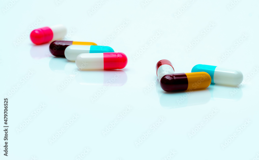 Multi-color antibiotic capsule pills spread on white background. Antibiotic drug resistance. Antimicrobial capsule pills. Pharmaceutical industry. Pink, white, blue, yellow, and red capsule pills. Multi-color antibiotic capsule pills spread on white background. Antibiotic drug resistance. Antimicrobial capsule pills. Pharmaceutical industry. Pink, white, blue, yellow, and red capsule pills.