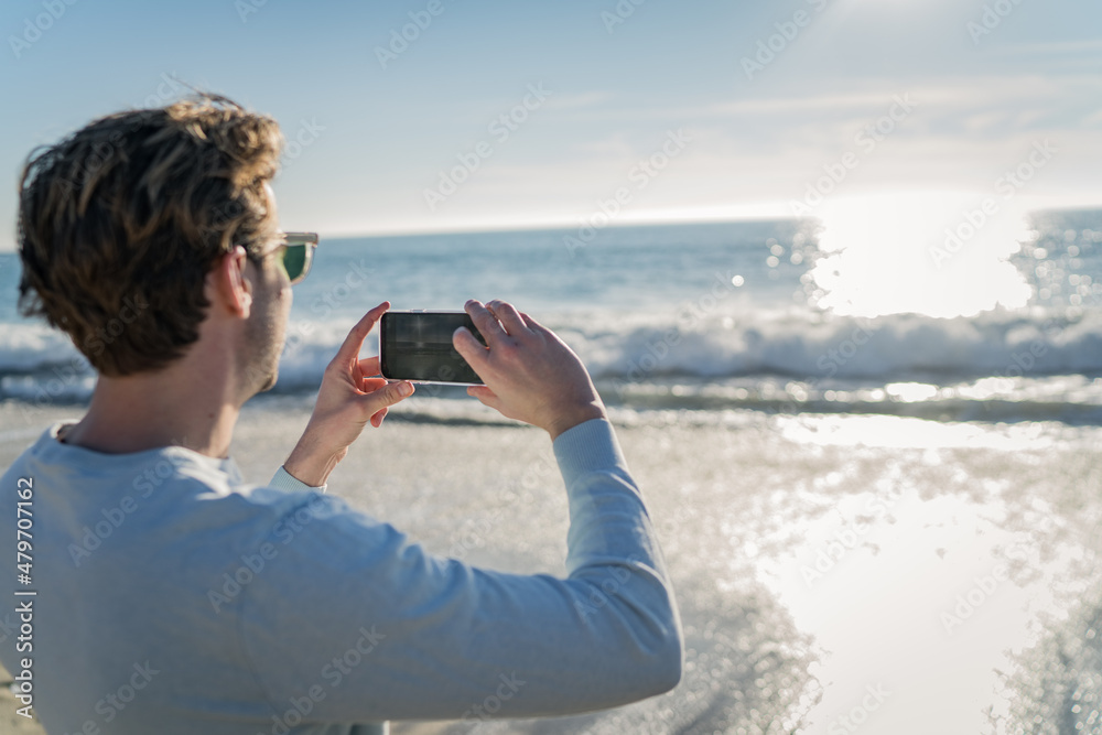 Man using a mobile phone on the beach for taking pictures