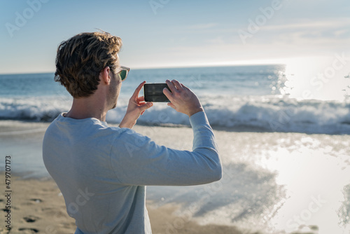 Man using a mobile phone on the beach for taking pictures