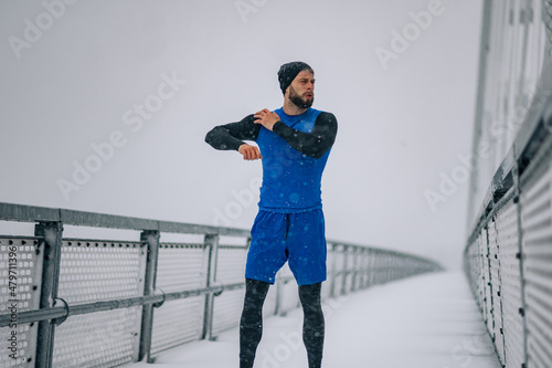 Man stretching before training on bridge during a winter snow day.