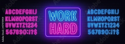 Work Hard neon lettering on brick wall background.