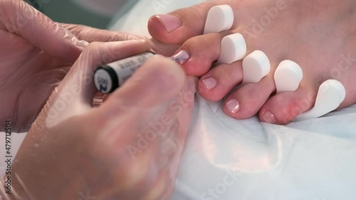 Pedicurist master is applying second coat of shiny soft pink gel shellac on woman's toes in beauty clinic, closeup view. Hygiene and care for feet. Professional pedicure in cosmetology clinic.