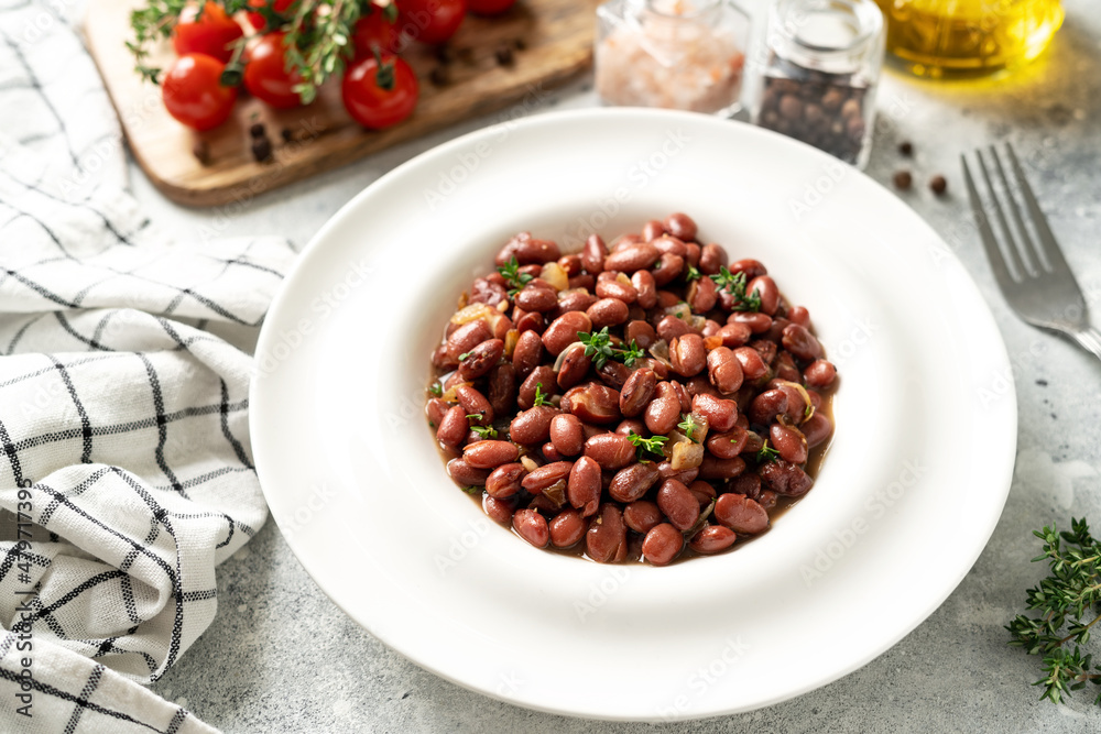 Stewed red beans with onion and thyme in tomato sauce in a white plate on the kitchen table closeup Stewed red beans with onion and thyme in tomato sauce in a white plate on the kitchen table closeup