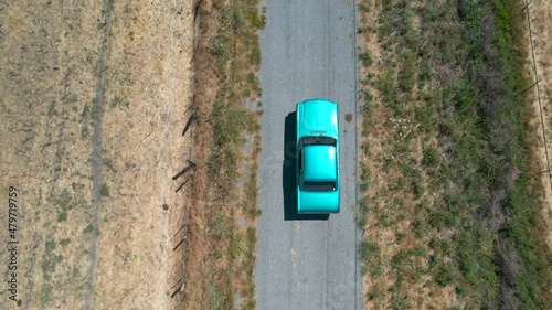 Drone footage of light blue classic mustant driving down rural country roads in California, during the day.