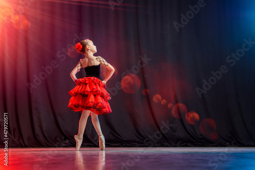 A little girl ballerina is dancing on stage in a tutu on pointe shoes with castanedas, the classic variation of Kitri. photo