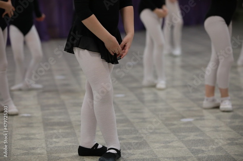 Female legs and arms in the position of a young dancer at a lesson in the gymnasium of a dance school for girls children