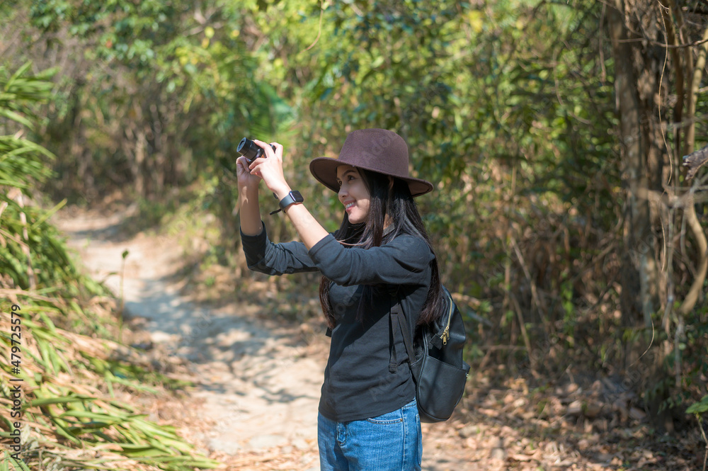 Naklejka premium Young woman trekker taking photos of nature with camera in the woods, holidays and traveling concept.