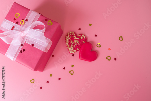 Female hands are holding a box with a gift near the decorative hearts on white background, top view