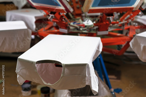 a white t-shirt on wooden shelve of the print screening apparatus. serigraphy production. printing images on t-shirts