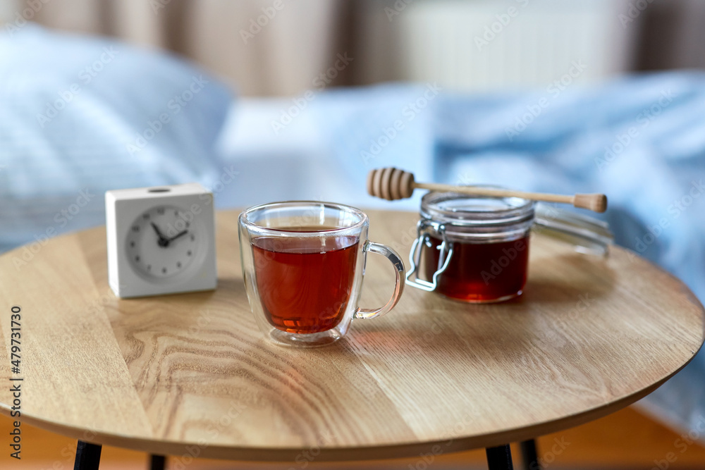 sleep disorder, bedtime and morning concept - close up of cup of relaxing tea, honey and alarm clock on night table at home sleep disorder, bedtime and morning concept - close up of cup of relaxing tea, honey and alarm clock on night table at home