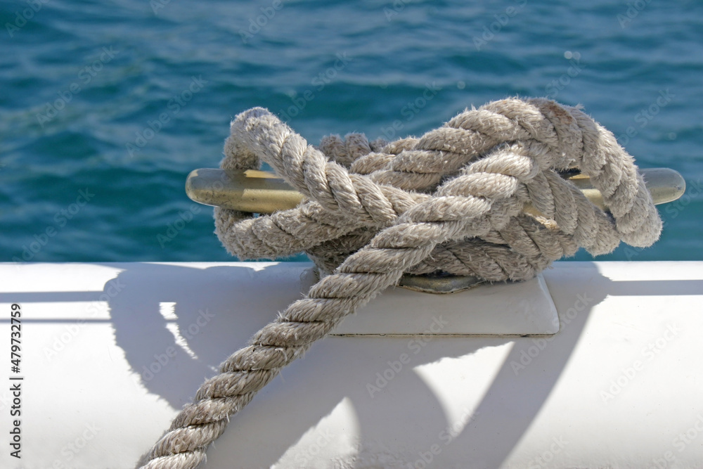 Fototapeta premium Rope tied securely around a meatal boat cleat in a nautical knot. Background of blue ocean water.
