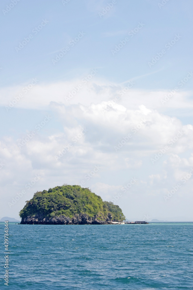Single round forested island in the ocean with small boat moored against a summer sky background Single round forested island in the ocean with small boat moored against a summer sky background