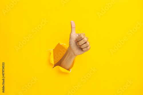 Close-up of male hand showing thumbs up on yellow background. photo