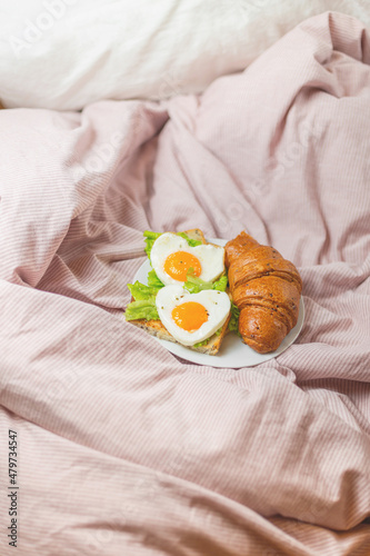 Two eggs on toast with lettuce and croissant on pink pastel linen. Romantic breakfast service. Heart-shaped scrambled eggs with fresh pastries. Concept for February 14