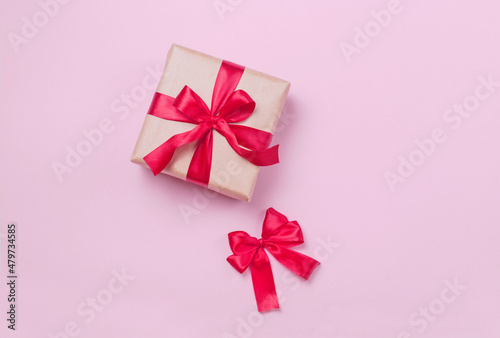 Cardboard packaging of a festive gift with a red beautiful bow. Eco gift wrapping made of paper with a ribbon on a pink background. Beautiful banner for the Valentine's Day