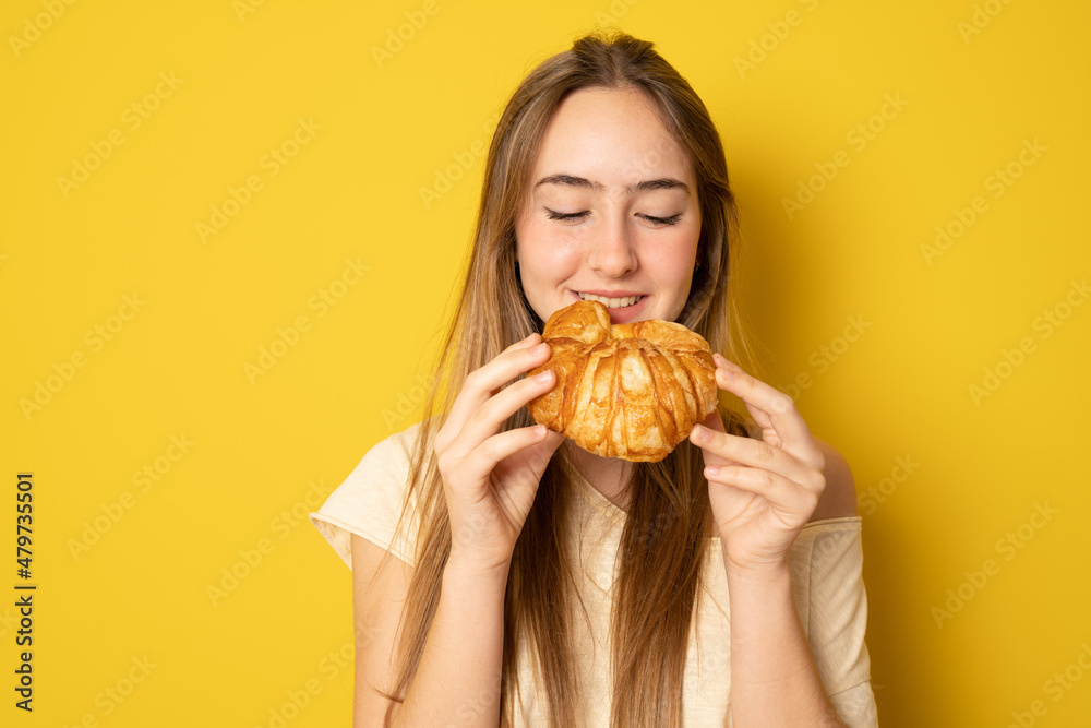 Young woman eating croissant, coffee break. Isolated over yellow background. Diet concept.