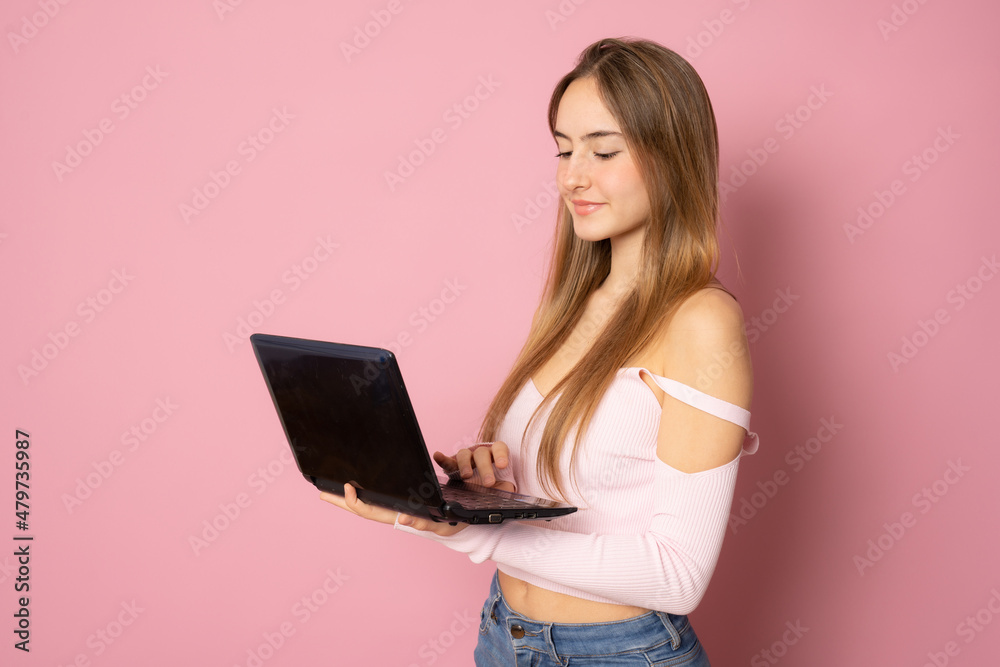 Beautiful girl with long hair using laptop computer standing isolated over pink background.