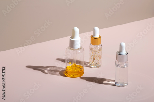 Natural skin care cosmetic in dropper bottles oil, golden serum, hyaluronic, squalane, collagen with hard shadows on pastel neutral pink background