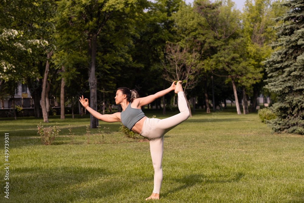 Young female practising yoga in public park at sunrise