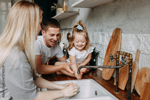 A happy family with a child having fun washing dishes and splashing water in the kitchen at home. Funny emotional mom dad and daughter are getting ready for dinner this weekend. Selective focus