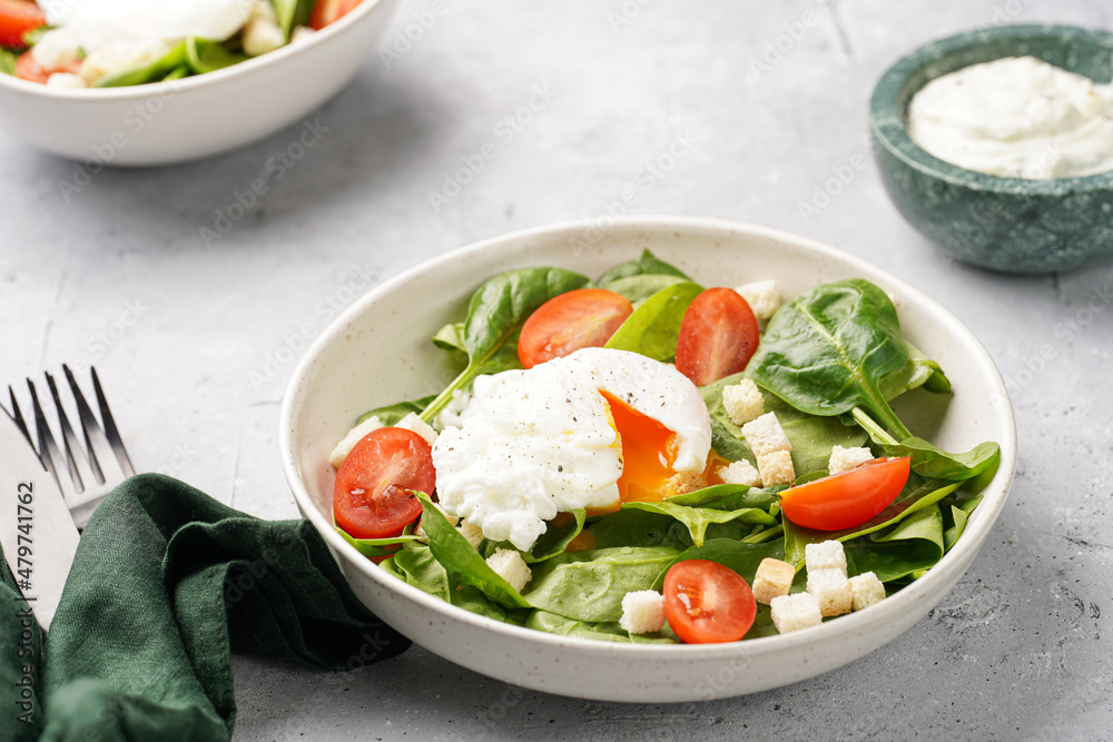 Salad bowl with fresh green spinach, cherry tomatoes, croutons, egg benedict and sour cream dressing on a grey stone surface Salad bowl with fresh green spinach, cherry tomatoes, croutons, egg benedict and sour cream dressing on a grey stone surface