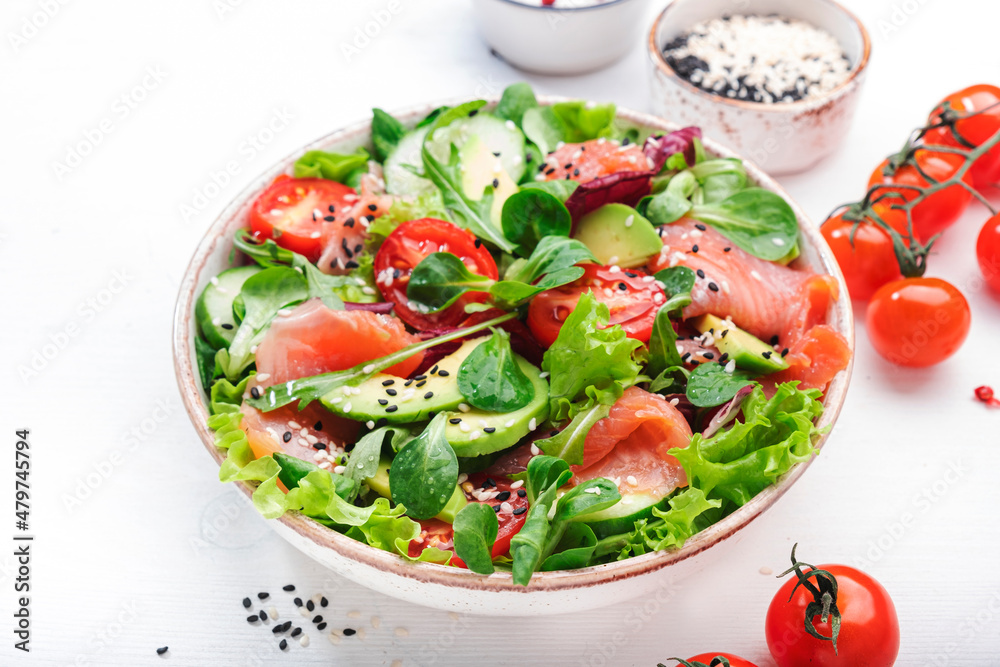 Spring salad with salted salmon, avocado, tomatoes, cucumber, black sesame seeds, olive oil, and mixed herbs. White background, top view, copy space Spring salad with salted salmon, avocado, tomatoes, cucumber, black sesame seeds, olive oil, and mixed herbs. White background, top view, copy space